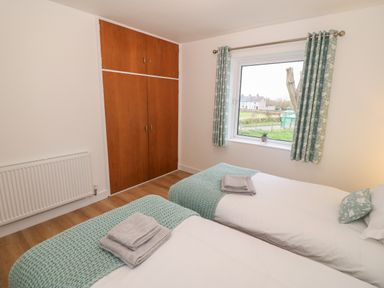 A bedroom with two single beds having teal blankets and towels with a wooden closet and window with curtains at Berth in Afonwen near Criccieth