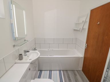 A bathroom with a bathtub sink mirror wooden door and striped rug at Berth in Afonwen near Criccieth