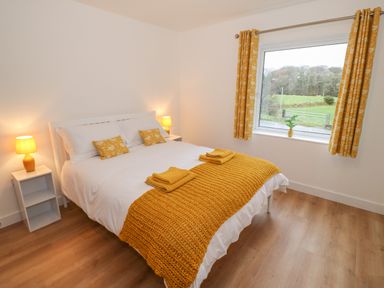 A bedroom with a white bed having yellow blanket pillows and towels two bedside tables with lamps and a window with yellow curtains at Berth in Afonwen near Criccieth