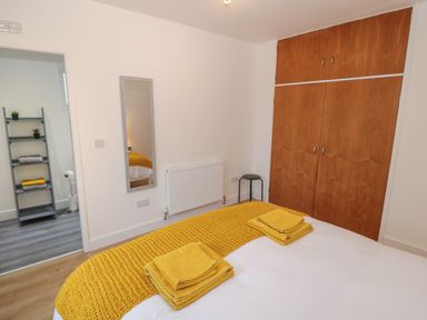 A bedroom with a bed covered in yellow blankets and towels wooden wardrobe a mirror and view to an adjoining room with shelves at Berth in Afonwen near Criccieth