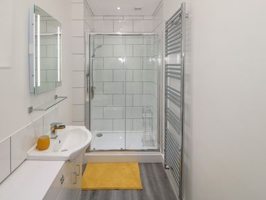A bathroom with a sink mirror and shower enclosure with yellow bath mat at Berth in Afonwen near Criccieth