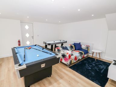 A game room with a pool table air hockey table a colorful sofa a small round table and a dark rug at Berth in Afonwen near Criccieth