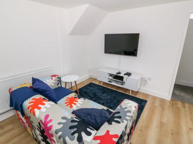 A living room with a colorful patterned sofa a white TV stand with electronics and a wall-mounted TV at Berth in Afonwen near Criccieth