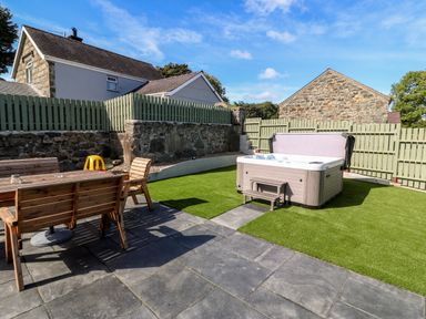 A garden with a hot tub and wooden table with chairs at Berth in Afonwen near Criccieth