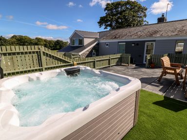 An outdoor patio area with a hot tub wooden chairs a fence and a single story building at Berth in Afonwen near Criccieth