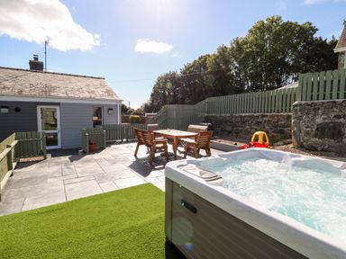 An outdoor patio area with a hot tub wooden table and benches enclosed by a wooden fence at Berth in Afonwen near Criccieth