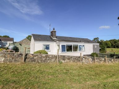 A single-story house with a stone wall and fenced grass area at Berth in Afonwen near Criccieth