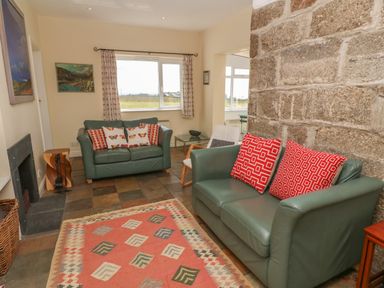 A living room with two green leather sofas with red patterned cushions and a patterned rug on a tiled floor at Rospletha Bungalow in Treen