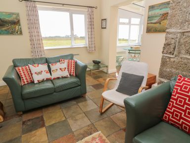 A living room with green sofas decorated with cushions and a white armchair next to a stone wall at Rospletha Bungalow in Treen
