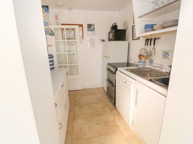 A narrow kitchen with white cabinets a stove a dishwasher a sink and a refrigerator at Rospletha Bungalow in Treen