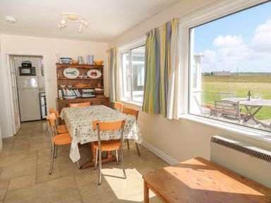 A dining room with a table and chairs next to large windows with a view of the outdoor patio at Rospletha Bungalow in Treen