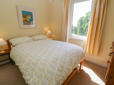 A bedroom with a double bed two bedside tables with lamps a framed picture on the wall and a window with yellow striped curtains at Rospletha Bungalow in Treen