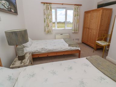 A bedroom with two single beds a wooden wardrobe a yellow chair and a window showing an outdoor view at Rospletha Bungalow in Treen
