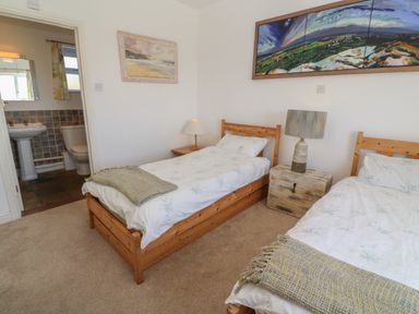 A bedroom with two single wooden beds a bedside table with a lamp a painting on the wall and an adjoining bathroom at Rospletha Bungalow in Treen