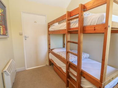 A bedroom with wooden bunk beds a heater on the wall and a painting by the door at Rospletha Bungalow in Treen