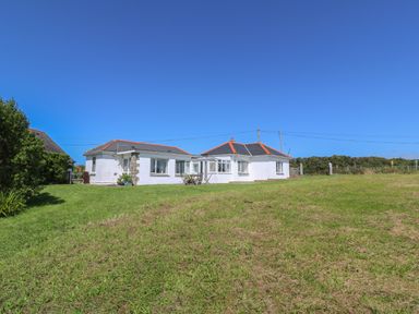 A white bungalow with a red roof on a grassy lawn under a blue sky at Rospletha Bungalow in Treen