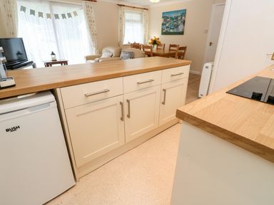 A kitchen with white cabinets and wooden countertops overlooking a living area with a dining table and chairs at 17 River Banks in Liskeard
