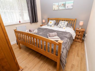 A bedroom with a wooden bed frame a gray blanket floral pillows two bedside tables with lamps and a wooden floor at 17 River Banks in Liskeard