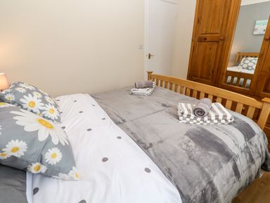 A bedroom with a wooden bed frame and a wooden wardrobe with mirrored doors at 17 River Banks in Liskeard