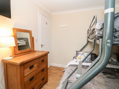 A room with a wooden dresser with a mirror and lamp next to a metal bunk bed at 17 River Banks in Liskeard