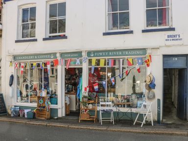 A street view of a shop with nautical flags hanging outside and chairs with hats displayed at 17 River Banks in Liskeard