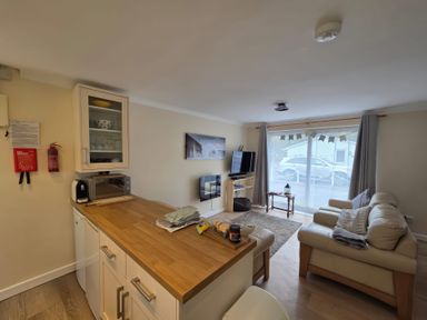 A living area with a wooden countertop, white cabinets, a television, and beige sofas near sliding glass doors at 17 River Banks in Liskeard