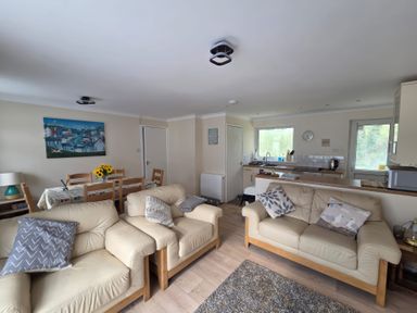 An open living room and kitchen area with cream sofas and wooden dining table at 17 River Banks in Liskeard