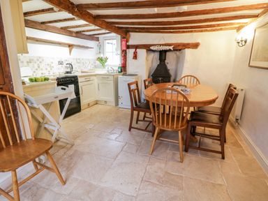 A kitchen and dining area with wooden chairs around a table and a wood stove at Teign Cottage in Shaldon