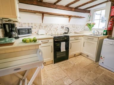A kitchen with an oven coffee maker microwave toaster and sink with flowers on the counter at Teign Cottage in Shaldon