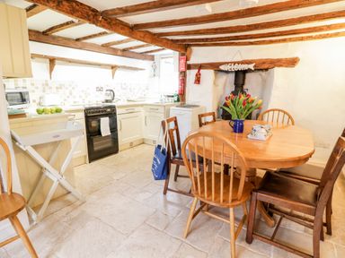A kitchen with wooden beams a round dining table chairs a stove and a vase of tulips at Teign Cottage in Shaldon