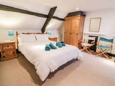 A bedroom with a double bed with white bedding two wooden bedside tables with lamps a wooden wardrobe two chairs and a mirror above a fireplace at Teign Cottage in Shaldon