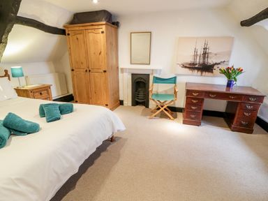 A bedroom with a bed with teal towels a wooden wardrobe a desk with flowers a chair and a small fireplace at Teign Cottage in Shaldon
