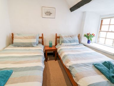 A bedroom with two single beds a small wooden table and a window with flowers at Teign Cottage in Shaldon