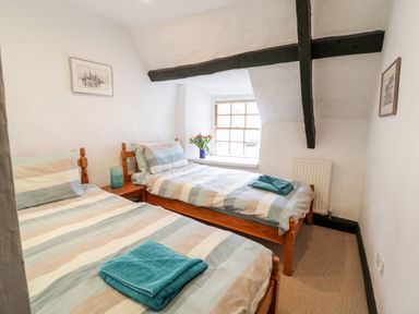 A bedroom with two single beds a wooden window and exposed ceiling beams at Teign Cottage in Shaldon