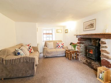 A living room with two sofas a stone fireplace with a wood stove and wooden side tables at Teign Cottage in Shaldon