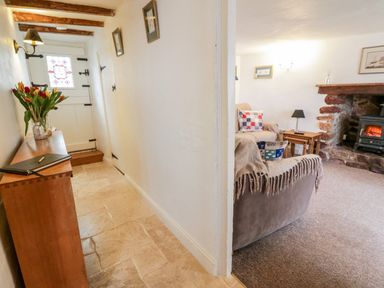 A hallway with a wooden console table and flowers next to a living room with sofas a side table and a fireplace at Teign Cottage in Shaldon