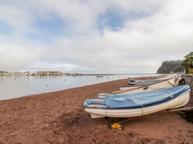 A beach with several boats covered with tarps lined up next to the water at Teign Cottage in Shaldon