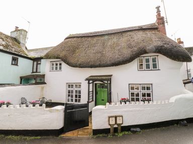A white thatched cottage with a small black gated patio and pink flowers at Teign Cottage in Shaldon