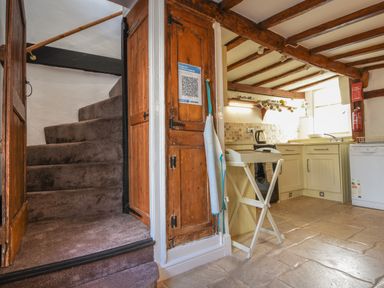 A kitchen with cream cabinets a dishwasher and a staircase with carpet at Teign Cottage in Shaldon