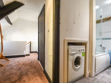 A hallway with carpet and wooden door leading to a bathroom with a bathtub and washing machine at Teign Cottage in Shaldon