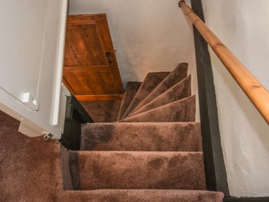 Carpeted narrow staircase with wooden handrail and wooden door at the top at Teign Cottage in Shaldon
