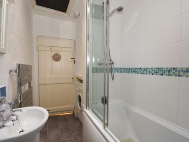 A bathroom with a sink towel rack washing machine bathtub and shower at Teign Cottage in Shaldon