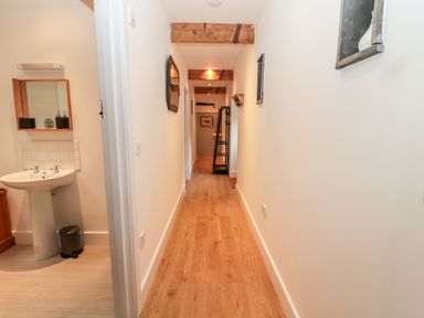 A narrow hallway with wooden floor and white walls with a pedestal sink bathroom on the left at The Old Workshop Middleton near Belford