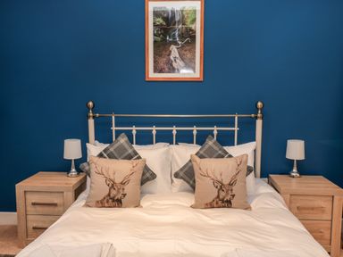 A bedroom with a white metal bed frame blue wall two pine bedside tables and two lamps at The Old Workshop in Middleton near Belford