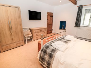 A bedroom with a bed folded towels a wooden wardrobe dresser chair wall mounted tv window and wooden door at The Old Workshop in Middleton near Belford