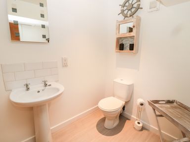 A bathroom with a pedestal sink mirror toilet and wooden shelf with toiletries at The Old Workshop in Middleton near Belford