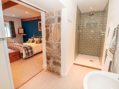 A bedroom with a bed and plaid curtains next to a bathroom with a tiled shower area at The Old Workshop in Middleton near Belford