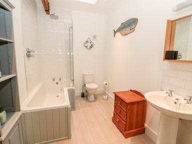 A bathroom with a bathtub, toilet, wooden cabinet, sink, and a decorative fish on the wall at The Old Workshop in Middleton near Belford