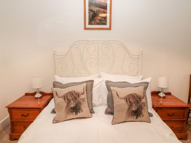 A bedroom with a white metal bed frame wooden bedside tables with lamps and cushions with a bull design at The Old Workshop in Middleton near Belford