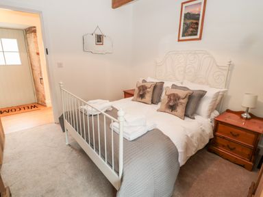 A bedroom with a white metal bed frame two wooden bedside tables and a welcome mat by the door at The Old Workshop in Middleton near Belford